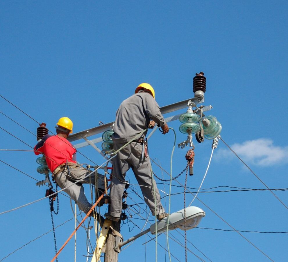 Two linesmen in hard hats working on overhead power lines and insulators