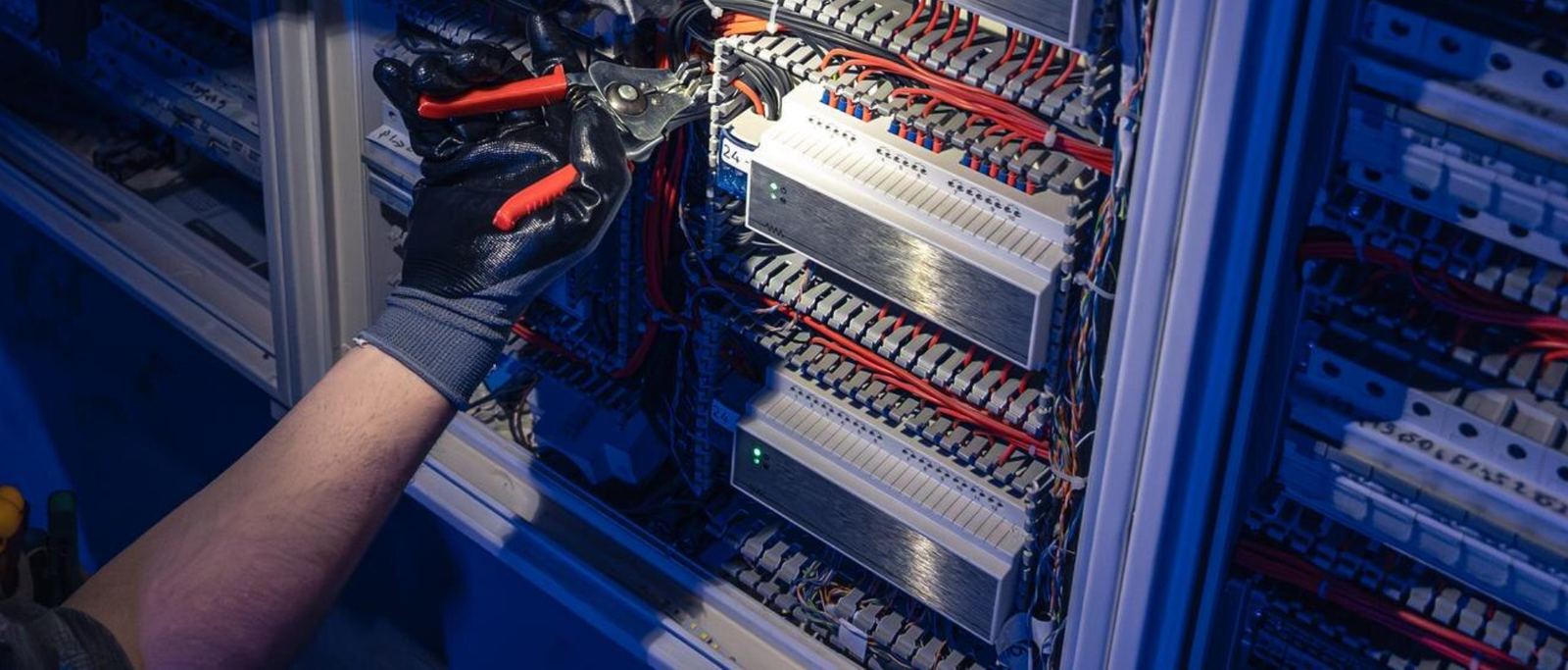 Gloved hand using pliers inside a densely wired control panel