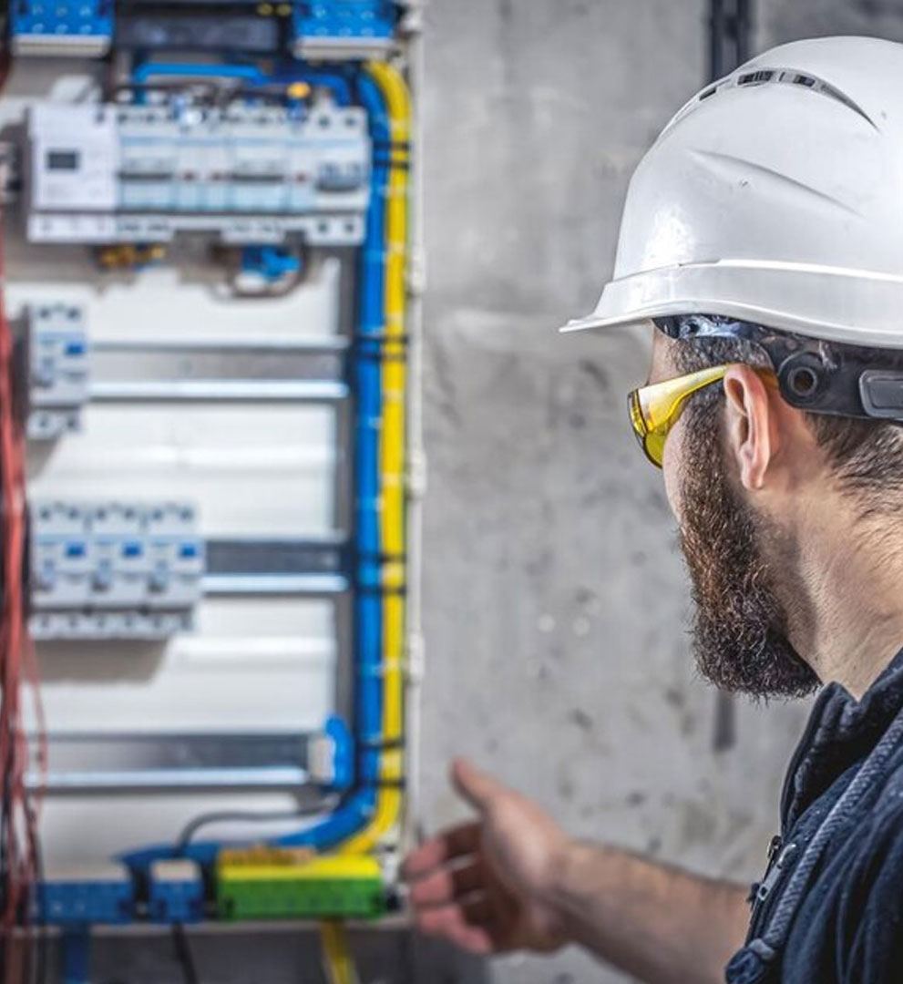 Electrician in hard hat and safety glasses studying a distribution board