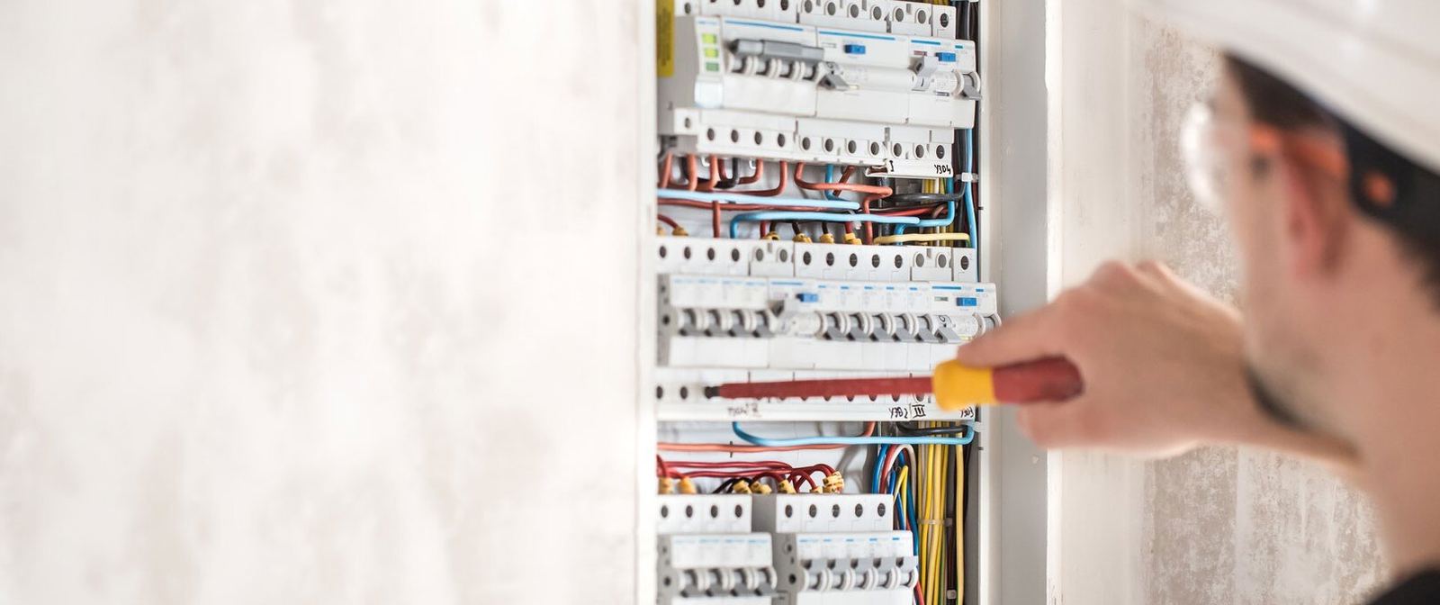 Electrician in hard hat testing a densely populated distribution board with an insulated screwdriver