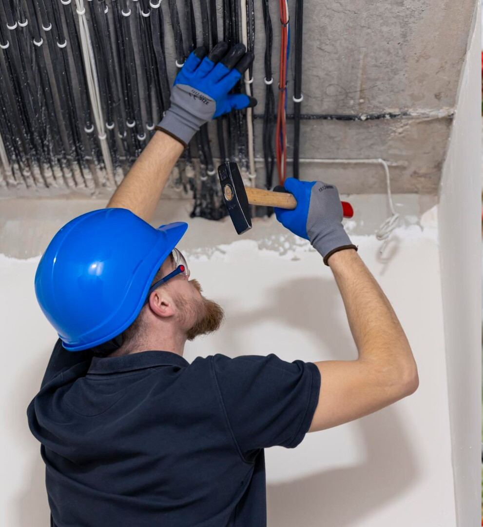 Electrician in hard hat clipping cable runs to a concrete ceiling