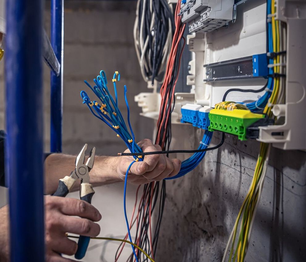 Ferruled blue conductors and pliers held beside an open distribution board