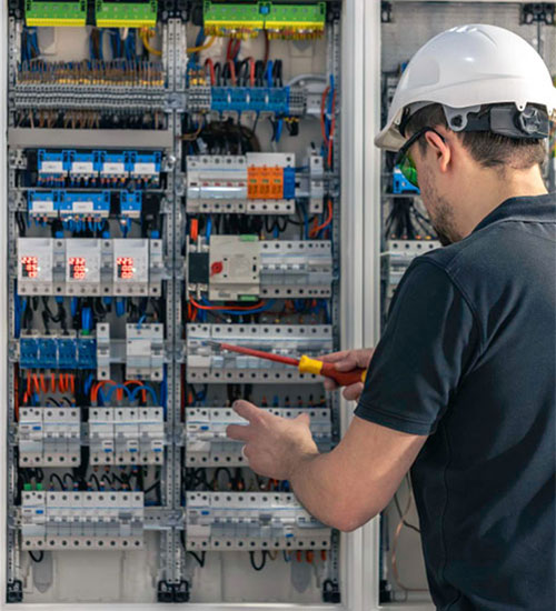 Hard-hatted electrician working at a large commercial three-phase distribution panel