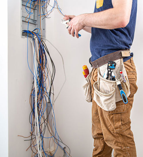 Electrician in a tool belt wiring a consumer unit, cables hanging loose