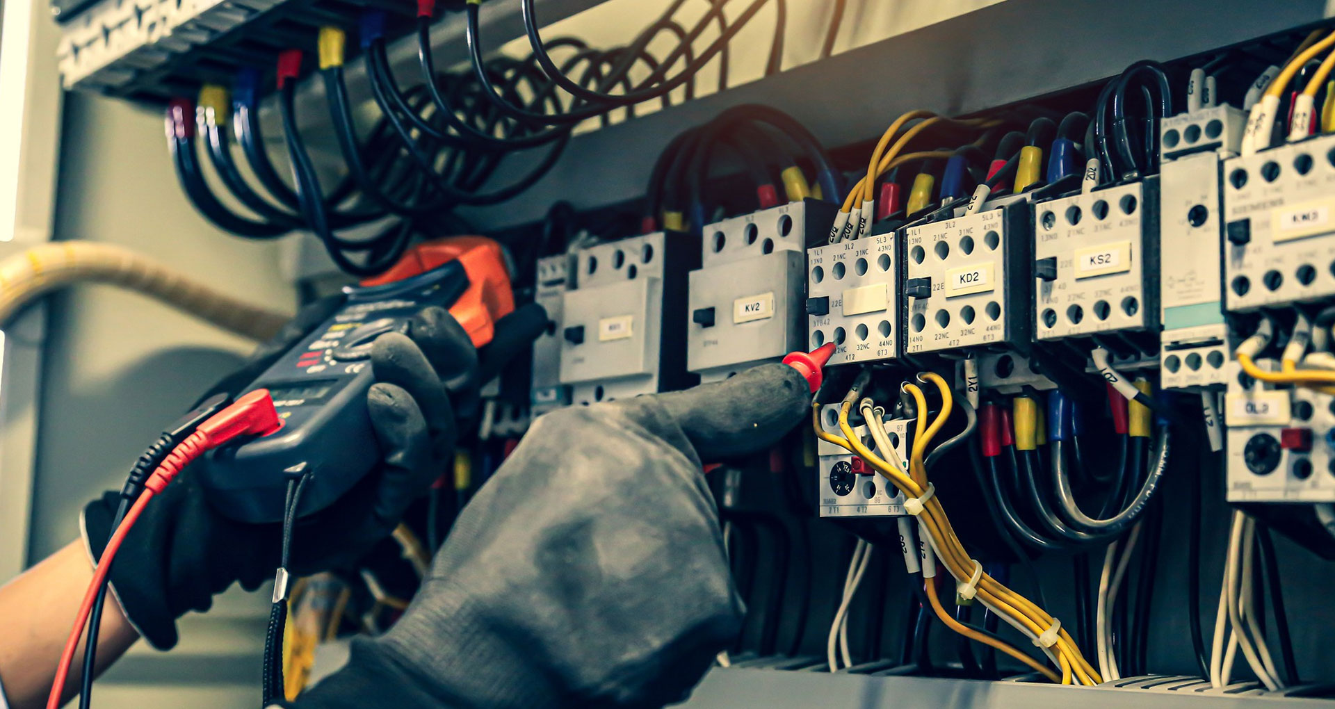 Gloved hands testing wired contactors in a control panel with a multimeter