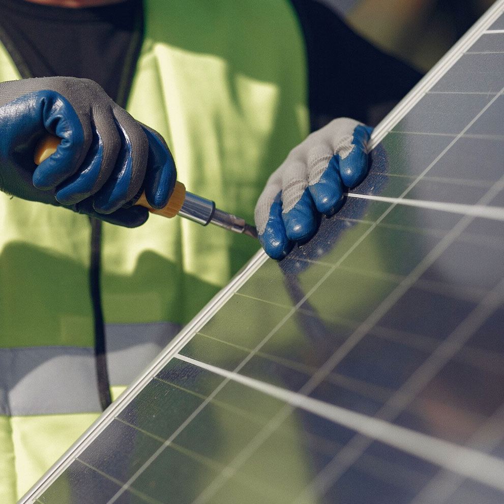Gloved installer in hi-vis fixing a solar panel frame with a screwdriver