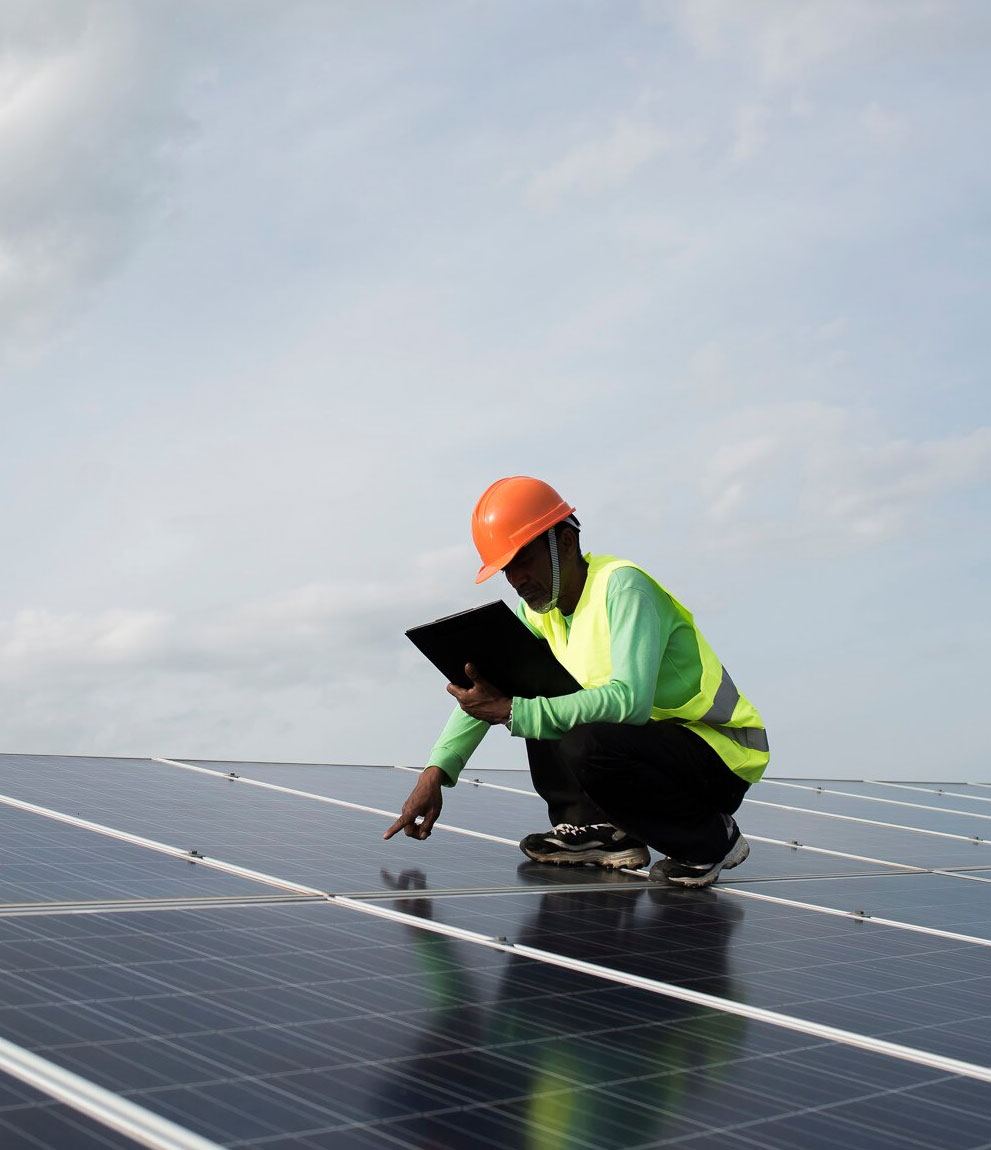 Engineer crouching on a large solar array, inspecting panels with a folder